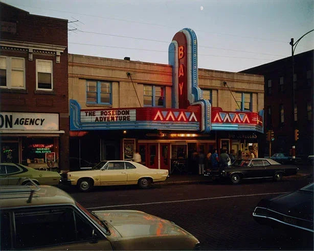Archival color photo of The Bay Theater marquee illuminated at dusk in the 1970s, featuring 'The Poseidon Adventure' and vintage cars.