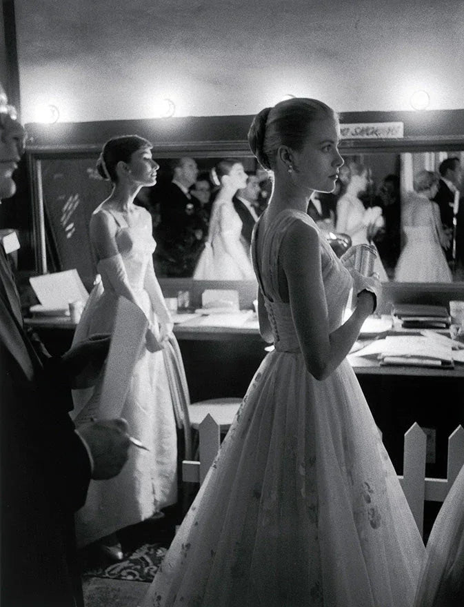 Black and white backstage scene at an awards event with women in elegant gowns preparing by a mirror