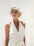 Emotional portrait of a woman styled as Marilyn Monroe, wearing a white halter dress with a distressed expression against a bright white wall.