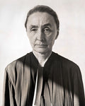 Black and white portrait of a serious elderly woman wearing a dark robe against a plain background