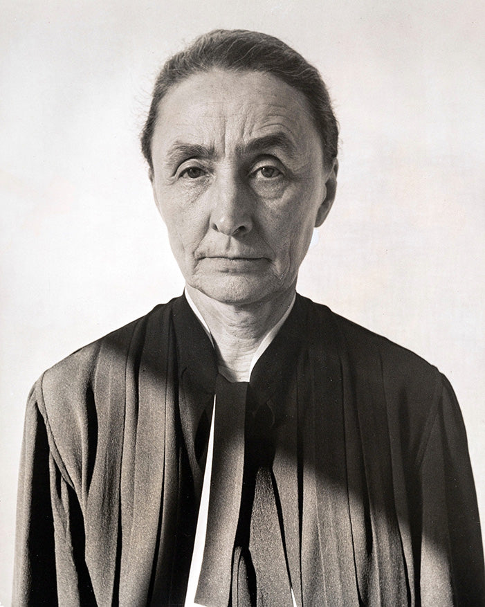 Black and white portrait of a serious elderly woman wearing a dark robe against a plain background