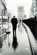 Black and white photo of James Dean walking alone on rainy Times Square sidewalk in 1955