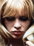 Close-up portrait of a blonde woman with long hair and bangs looking down with closed lips