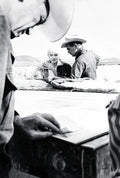 Black and white photo on the set of The Misfits featuring Marilyn Monroe and two men in cowboy hats in a desert setting