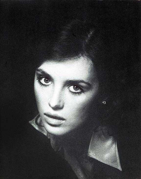 Dramatic close-up black and white portrait of a young Cher with intense eyes and high-collared shirt, classic 1970s celebrity photo.