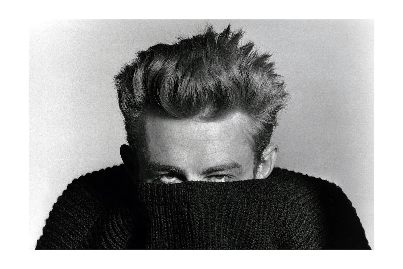 Black and white close-up portrait of a man with styled hair partially covering face with a black knitted sweater