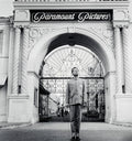 Black and white photo of a man in uniform standing in front of ornate Paramount Pictures entrance gate in Los Angeles