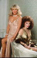 Full-color studio portrait of Linda Evans in a shimmering pink sequin dress and Joan Collins in a gold gown, showcasing 80s Dynasty style.