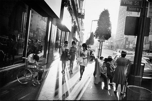High contrast black and white photo of 1960s mod women walking on sunny Vine Street in Hollywood, CA, with strong shadows and reflections.