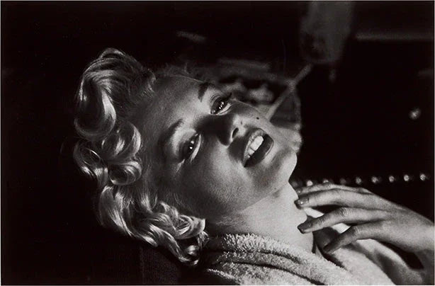 Black and white close-up portrait of Marilyn Monroe looking up, showing her classic curls and hand resting on her neck, emphasizing cinematic glamour.