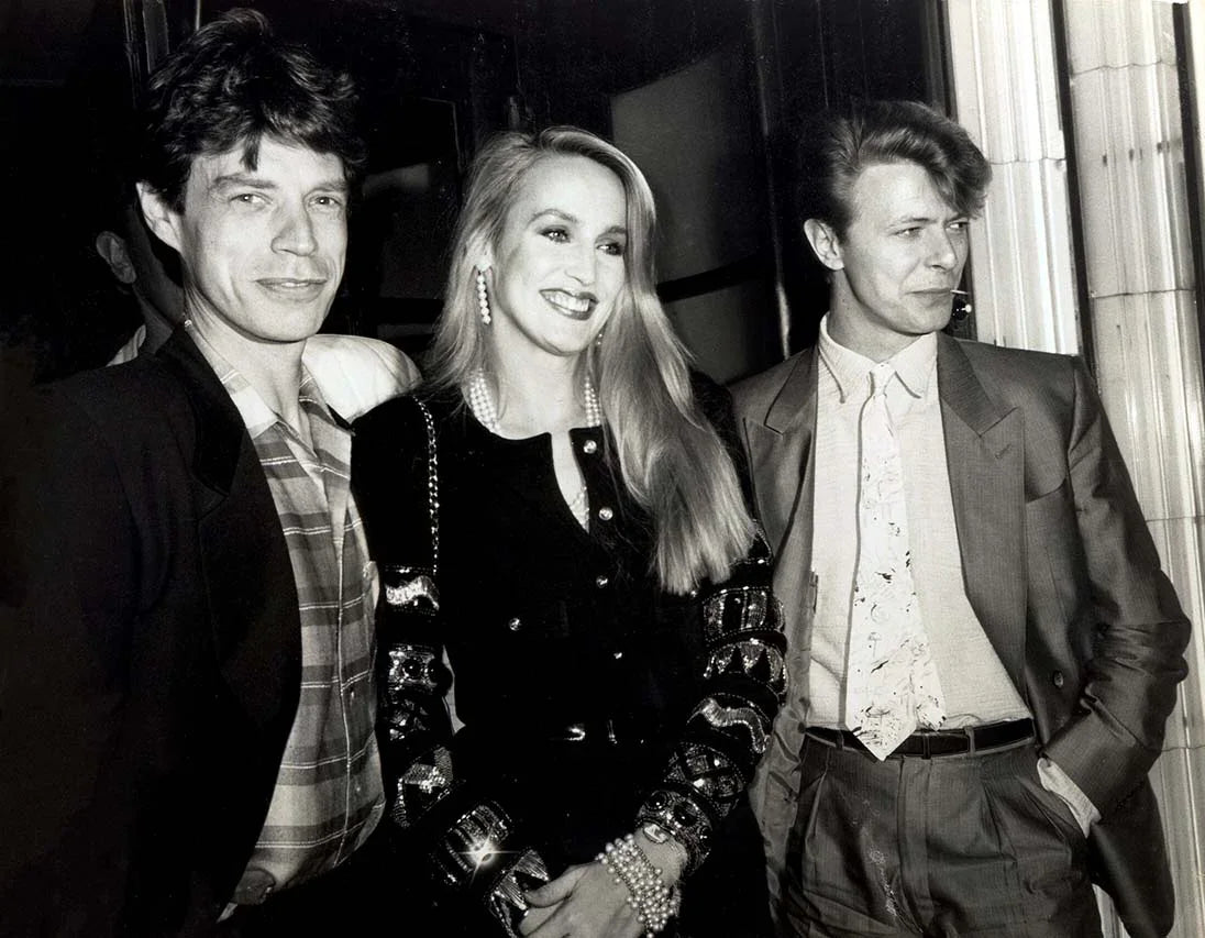 Black and white photo print showing Mick Jagger, Jerri Hall, and David Bowie at a 1984 birthday celebration in London.