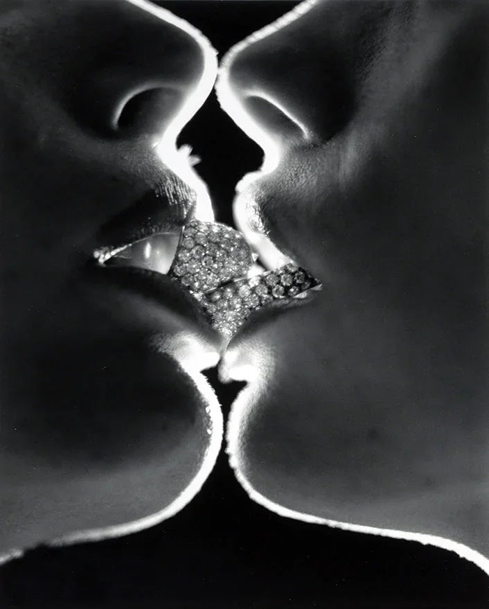 Dramatic black and white photograph by Helmut Newton showing two faces kissing, separated by a sparkling diamond cluster jewel.