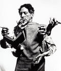 Black and white portrait of Jean Cocteau with multiple hands holding a book, pen, and cigarette, photographed by Philippe Halsman.