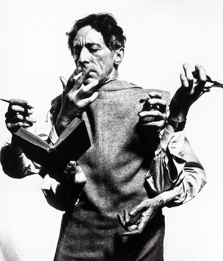 Black and white portrait of Jean Cocteau with multiple hands holding a book, pen, and cigarette, photographed by Philippe Halsman.