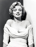Black and white portrait of Marilyn Monroe in a ruched off-shoulder white dress with a brooch, smiling