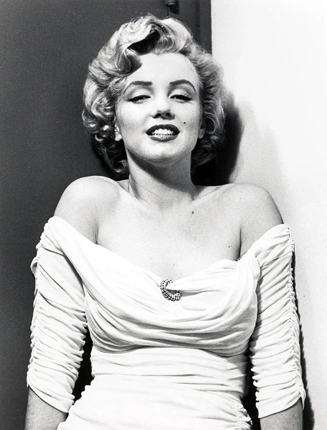 Black and white portrait of Marilyn Monroe in a ruched off-shoulder white dress with a brooch, smiling
