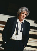 Richard Gere looking directly at the camera, wearing a black tuxedo jacket, white shirt, and an undone black bowtie, standing under dramatic lighting.