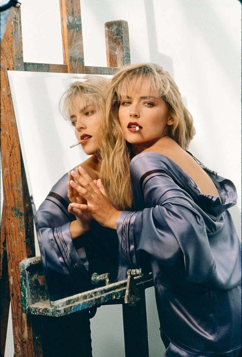 Iconic color portrait of actress Sharon Stone wearing a silk robe, smoking, and reflected in a mirror next to an artist's easel.