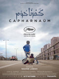 Official Capernaum movie poster showing a young boy pulling a smaller child in a cooking pot/makeshift cart on an elevated highway in a city setting under a cloudy sky.